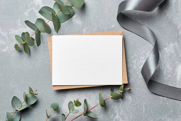 Greeting card mockup with copy space, envelope and eucalyptus twigs on grey concrete background — Stockfoto