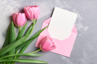 Üzerinde pembe zarf ve lale çiçekleri olan tebrik kartı modeli gri beton arka plan, üst manzara, kopyalama alanı