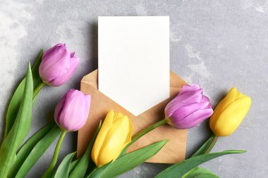 Gri arkaplanlı lale çiçekleri ve zarf içeren tebrik kartı modeli, üst görünüm, boşluğu kopyala