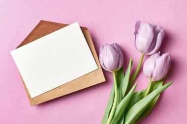 Zarflı tebrik kartı modeli ve pembe arka planda lale çiçeği buketi, üst manzara, boşluğu kopyala