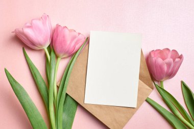 Zarflı tebrik kartı modeli ve pembe arka planda lale çiçekleri, üst görünüm, boşluk kopyala