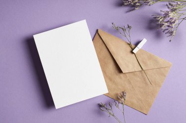 Lavanta rengi arka plan, üst görünüm, kopyalama alanı üzerinde zarf ve kuru limonyum çiçekleri içeren davetiye veya tebrik kartı modeli