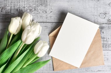 Zarflı tebrik kartı, fotokopi alanı ve ahşap arka planda lale çiçeği buketi, üst manzara