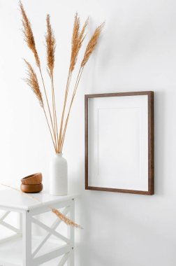 Resim, fotoğraf ve baskı sunumu için portre ahşap çerçeve modeli. İçi mobilya ve kuru çimen dekorasyonlarıyla dolu beyaz duvar..