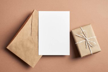 Kağıt zemin üzerinde zarf ve hediye kutusuyla davetiye veya tebrik kartı maketi
