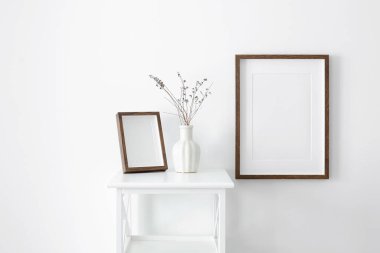 Resim, fotoğraf ya da baskı sunumu için portre ahşap çerçeveler ve fotokopi alanı. Beyaz duvar iç mimarisi, mobilya ve vazo kuru bitki süslemeleri..