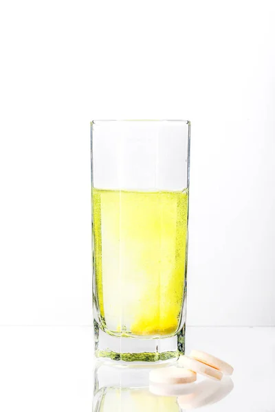 Beyaz arka planda bir bardak suda çözünen büyük, beyaz bir tablet. C vitamini.