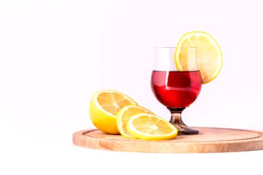 Kırmızı bir içecek ve beyaz arka planda limon dilimleri olan bir bardak..