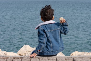 Küçük çocuğun sırtı Denize taş atıyor