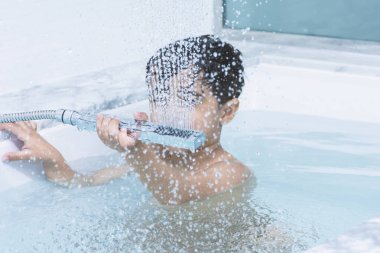 Küçük bir çocuk küvet suyunda duş alıyor.