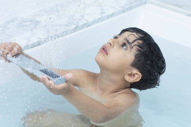 Küçük bir çocuk küvet suyunda duş alıyor.