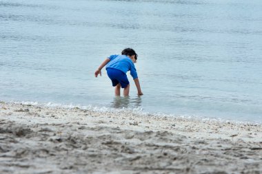 Kumsalda elini denize koyan küçük bir çocuk  