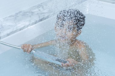 Küçük bir çocuk küvet suyunda duş alıyor.