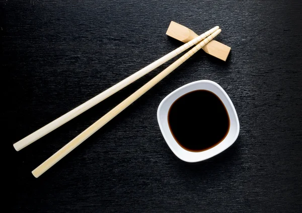 Japanse sushi stokjes over sojasaus kom, rijst op zwarte bac — Stockfoto