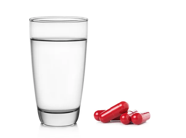 Glas Wasser und rote Tablettenkapseln auf weißem Hintergrund — Stockfoto