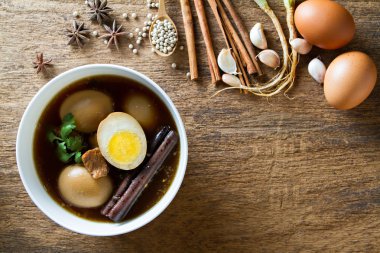 Eggs boiled in the gravy with spices on wooden background. Thai  clipart