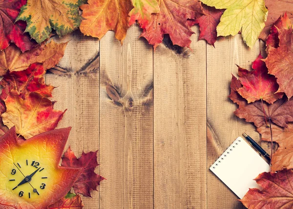 Still life of maple leaves, clock, notepad and pen on wooden pla — Stock Photo, Image