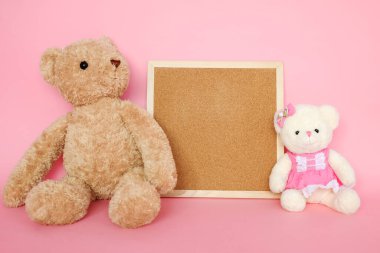 Pembe arka planda mantar tahtası olan birkaç oyuncak ayı.