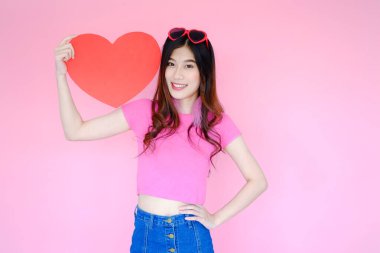Pembe arka planda güzel Asyalı kadın portresi, aşk konseptinde mutlu sevgililer günü, elinde kırmızı kalp işareti olan manken.
