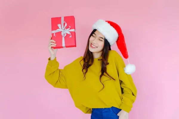 ポーズアジアの女性はピンクの背景に長い袖の服を着てサンタクロースの帽子と手に持っている赤いギフトボックス クリスマスやクリスマスの休日と幸せな新年のコンセプト 冬のファッション — ストック写真