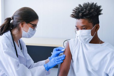 Kafkasyalı doktor kadın ya da hemşire hastanede ya da klinikte Afrikalı Amerikalı bir adama grip ya da antiviral aşı veriyor.