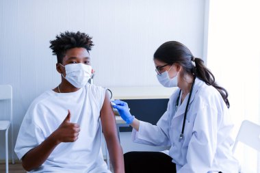 Kafkasyalı doktor kadın ya da hemşire hastanede ya da klinikte Afrikalı Amerikalı bir adama grip ya da antiviral aşı veriyor.