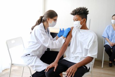 Kafkasyalı doktor kadın ya da hemşire hastanede ya da klinikte Afrikalı Amerikalı bir adama grip ya da antiviral aşı veriyor.