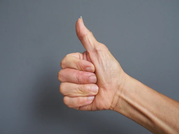 A hand making thumb up on gray background — Stock Photo, Image