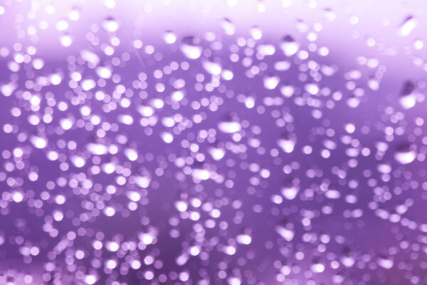 Nature bokeh, purple abstract rain drops on the window glass.