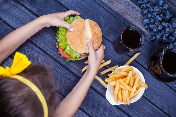 Child girl eating a burger fast food at the table. the view from the top — Stock Photo, Image