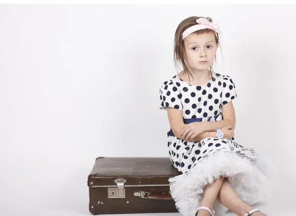 Menina sentada em uma mala velha — Fotografia de Stock