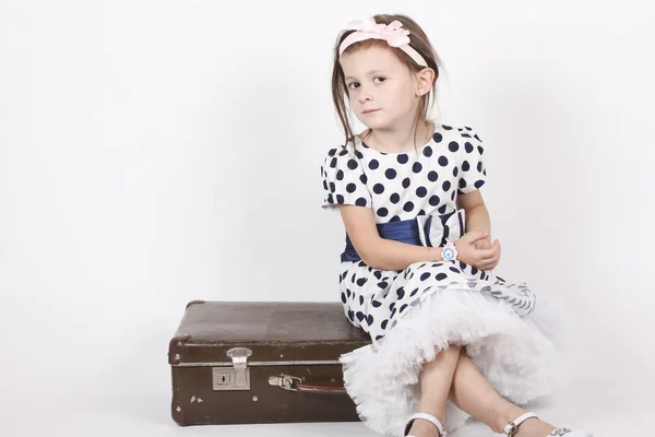 Menina sentada em uma mala velha — Fotografia de Stock