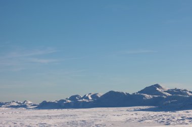 Kar çöl ve mavi kış gökyüzünde. Ufuktaki dağlar
