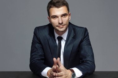 Masadaki resmi takım elbiseli bir iş adamının portresi, gri arka planda, stüdyoda izole edilmiş..