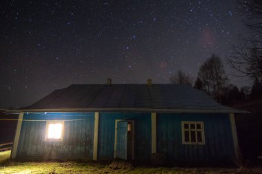 Geceleri dağlardaki yıldızlı gökyüzünün arka planında eski bir kır evi.