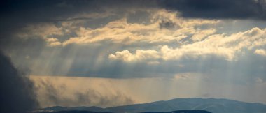 Güneş ışınları yazın Karpat dağlarının üzerinden bulutların arasından parlıyor.
