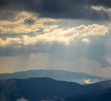 Güneş ışınları yazın Karpat dağlarının üzerinden bulutların arasından parlıyor.