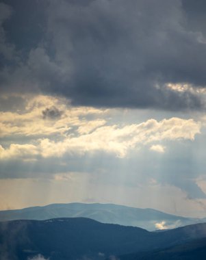 Güneş ışınları yazın Karpat dağlarının üzerinden bulutların arasından parlıyor.