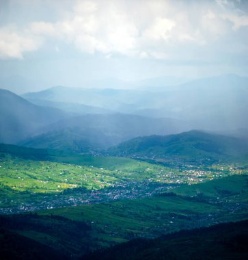 Karpat Dağları 'ndaki bir köy, ışık ışınları altında, yağmur bulutlarının arka planına karşı. Dinlen ve dağlarda dolaş. Güzel manzara.