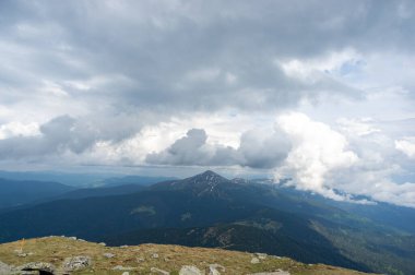Yazın başlarında, kar ve yeşil çimenlerin altında mavi gökyüzü ve beyaz bulutların ardında Hoverla Dağı.