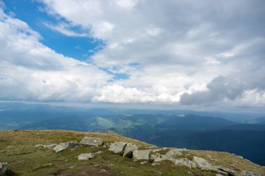 Yazın başlarında, kar ve yeşil çimenlerin altında mavi gökyüzü ve beyaz bulutların ardında Hoverla Dağı.