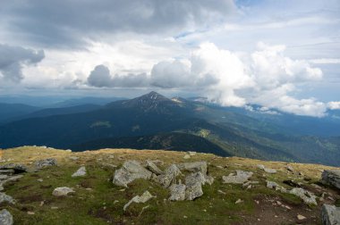 Yazın başlarında, kar ve yeşil çimenlerin altında mavi gökyüzü ve beyaz bulutların ardında Hoverla Dağı.