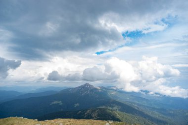 Yazın başlarında, kar ve yeşil çimenlerin altında mavi gökyüzü ve beyaz bulutların ardında Hoverla Dağı.
