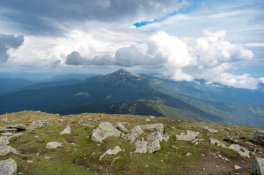 Yazın başlarında, kar ve yeşil çimenlerin altında mavi gökyüzü ve beyaz bulutların ardında Hoverla Dağı.