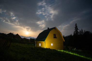 Night landscape, wooden house in a village near the forest in the Carpathian mountains in summer