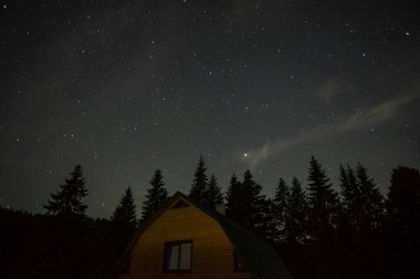 Beautiful night landscape, house among the forest against the background of the starry sky in the carpathians