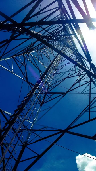 Tall metal tower with bouncing signal antennas, seen from the surface, with blue sky in the background and few clouds