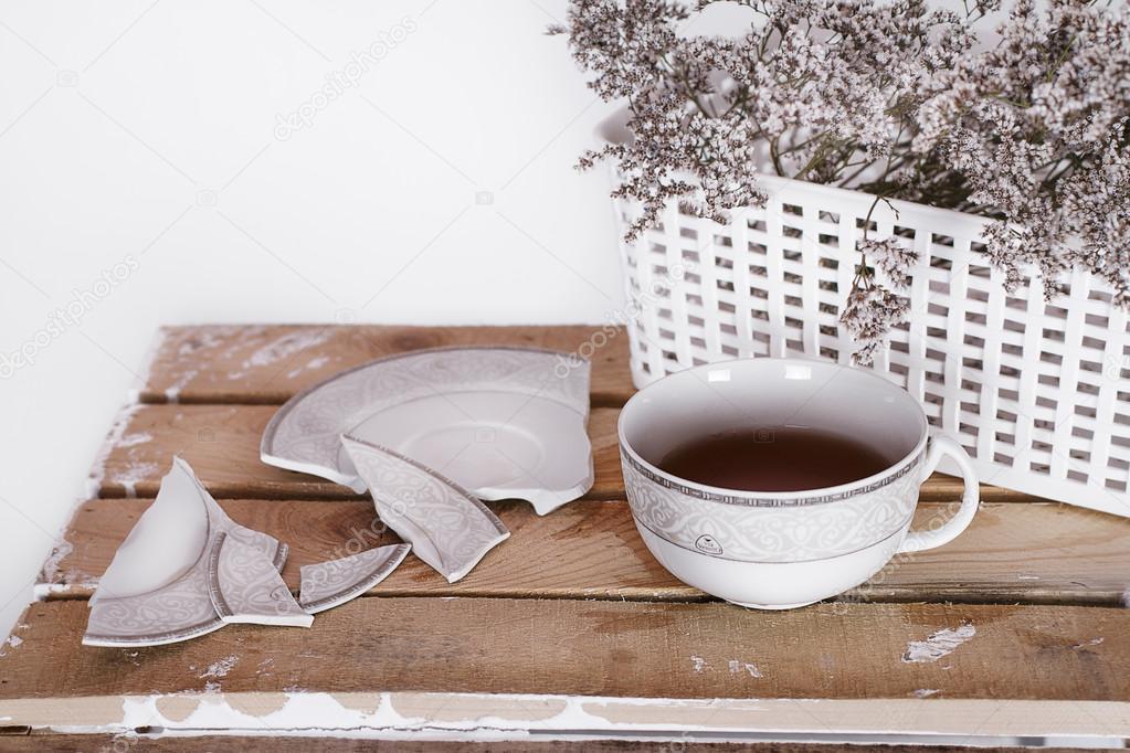 tea cup and saucer are broken near a basket with flowers