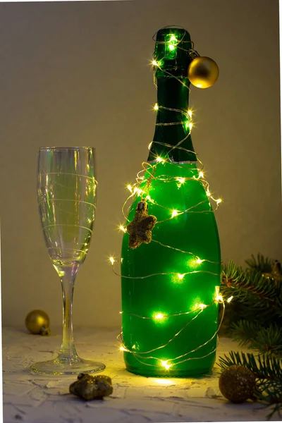 クリスマスツリーやガラスのような輝く庭に包まれた緑のシャンパンのボトル 白を背景に金の装飾と新年のコンセプト — ストック写真