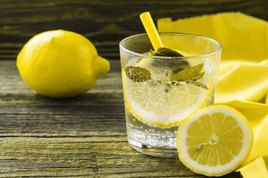 Limonata ya da limonlu mojito kokteyli ve buzlu nane. Soğuk yaz ferahlatıcı içeceği, ahşap arka planda sarı peçeteyle süslenmiş. 2021 Yılı Rengi
